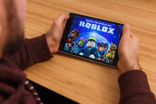 PRAGUE, CZECH REPUBLIC - MARCH 16, 2019: Man holding a smartphone and playng the Roblox mobile game. An illustrative editorial image on an bamboo background.