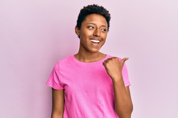 Young african american girl wearing casual clothes smiling with happy face looking and pointing to the side with thumb up.