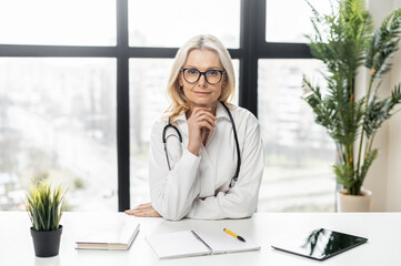 Headshot of confident middle-aged MD, pediatric, physician wearing white medical gown and...