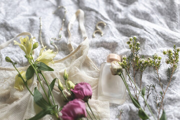 Stylish lingerie, modern jewelry, perfume bottle and spring flowers on bed. Soft trendy image