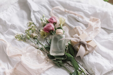 Stylish lingerie, gift, jewelry, perfume bottle and spring flowers on bed. Soft trendy image