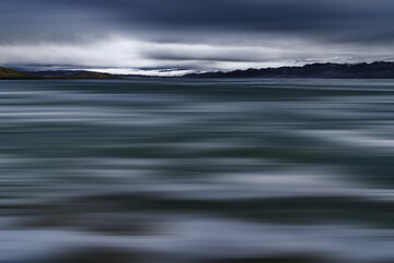Fototapeta na wymiar blurred view of sea surrounded by rocky coast with snow-covered summits