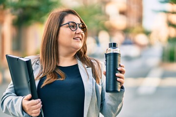 Young plus size businesswoman holding binder and bottle of water  at the city.