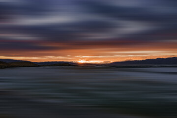 Fototapeta na wymiar blurred view of plain at root of snow-covered mountains at sunset 