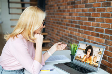 Video call concept. Two female colleagues speak online via video connection on the laptop. A middle-aged teacher has virtual conference with a student - obrazy, fototapety, plakaty