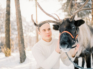 a man with a reindeer in a pine forest against a sunset background