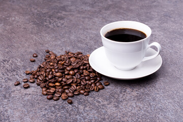 white porcelain cup with saucer full of hot coffee, with coffee beans beside