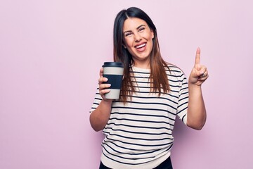 Young beautiful brunette woman drinking cup of takeaway coffee over isolated pink background smiling with an idea or question pointing finger with happy face, number one