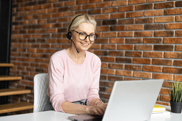 Online consultant in touch. A middle-aged woman wearing headset talking on the distance with a...