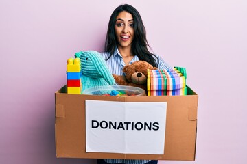 Beautiful hispanic woman holding donation box with toys celebrating crazy and amazed for success...