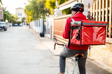 A courier on a bicycle with a red backpack wearing a mask and a helmet to deliver orders and packages for customers.
