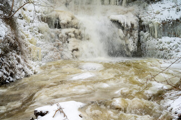 Winter Waterfall in Scenic Nature: Flowing Rapids and Icicles in a Snowy Brook