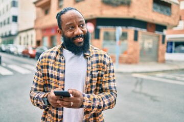 African american man with beard using smartphone typing and texting at the street with a happy smile