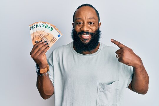 Young african american man holding bunch of 50 euro banknotes smiling happy pointing with hand and finger