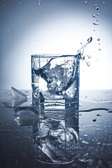 Water splash in glass with ice. On glossy background.