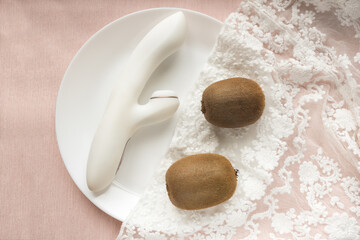 white silicone vibrator with vacuum mode on pink lace background with kiwi on the plat