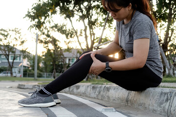 Concept of jogging, an Asian woman massaging her knees in a street sitting position.