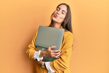 Fototapeta premium Young beautiful woman holding laptop looking at the camera blowing a kiss being lovely and sexy. love expression.