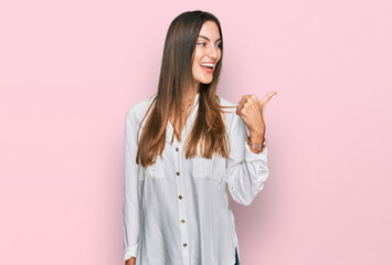 Young beautiful woman wearing casual clothes smiling with happy face looking and pointing to the side with thumb up.