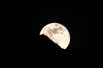 Luna llena saliendo por detrás de una montaña con la silueta de una casa  por detras