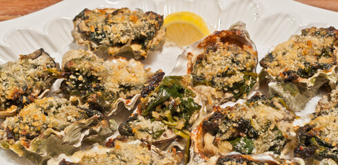 top view, close distance of a white dish of freshly prepared oysters Rockefeller, with slice of lemon