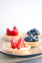 cake with cheese cream and fresh berries and wild berries on a beige plate on a wooden light background. Idea for culinary recipes and desserts. Perfect party concept