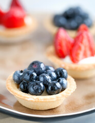 cake with cheese cream and fresh blueberries and wild berries on a beige plate on a wooden light background. Idea for culinary recipes and desserts. Perfect party individual fresh fruit dessert.
