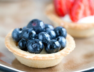 cake with cheese cream and fresh blueberries and wild berries on a beige plate on a wooden light background. Idea for culinary recipes and desserts. Perfect party individual fresh fruit dessert.