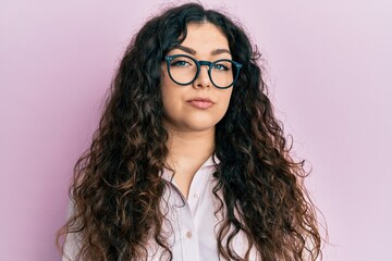 Obraz premium Young brunette woman with curly hair wearing casual clothes and glasses relaxed with serious expression on face. simple and natural looking at the camera.