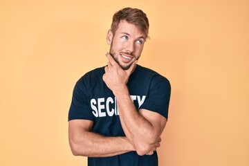 Young caucasian man wearing security t shirt with hand on chin thinking about question, pensive expression. smiling with thoughtful face. doubt concept.