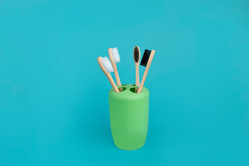 Family set of four bamboo toothbrushes in green toothbrush glass
on a blue background. Concept for a natural organic oral care product. No waste concept, no harm to nature. copy space.
