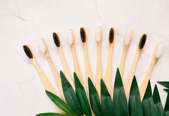 Lots of bamboo toothbrushes and green leaves on a white marble background with free space for text or message. Oral care concept. top view. Flat lay. copy space