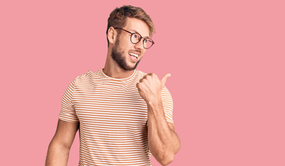 Young caucasian man wearing casual clothes and glasses smiling with happy face looking and pointing to the side with thumb up.