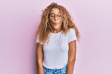 Beautiful caucasian teenager girl wearing white t-shirt over pink background making fish face with lips, crazy and comical gesture. funny expression.