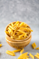 Uncooked yellow pasta in a wooden bowl on gray table. Selective focus. Italian food concept. Vertical orientation