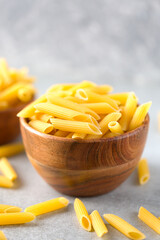 Uncooked yellow pasta in a wooden bowl on gray table. Selective focus. Italian food concept. Vertical orientation