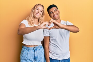 Young interracial couple wearing casual white tshirt smiling in love doing heart symbol shape with hands. romantic concept.