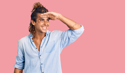 Young hispanic man wearing summer style very happy and smiling looking far away with hand over...