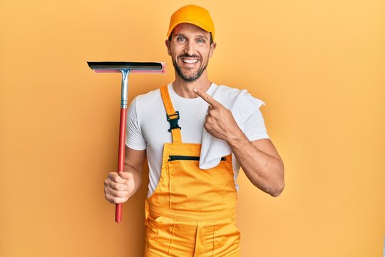 Young handsome man wearing glass clenaer uniform and squeegee smiling happy pointing with hand and finger