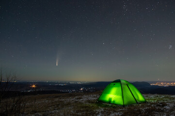 Winter tent in the mountains against the background of stars and comets