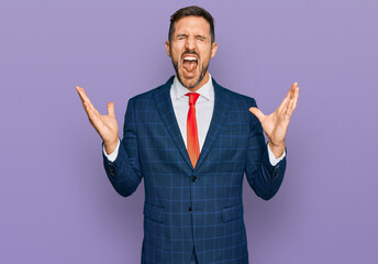 Handsome man with beard wearing business suit and tie celebrating mad and crazy for success with arms raised and closed eyes screaming excited. winner concept