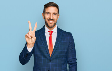 Handsome man with beard wearing business suit and tie showing and pointing up with fingers number two while smiling confident and happy.