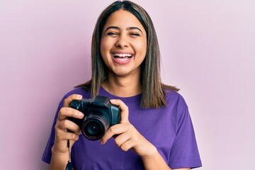 Young latin woman using reflex camera smiling and laughing hard out loud because funny crazy joke.