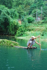 chinese rowing a bamboo boat full of bamboo down the river in front of a forest