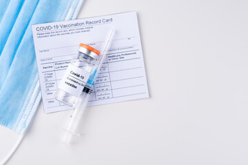 Covid-19 vaccine vial, vaccination record card, syringe, medical mask on a white background.