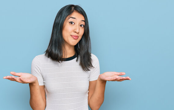 Beautiful asian young woman wearing casual white t shirt clueless and confused expression with arms and hands raised. doubt concept.