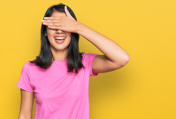 Beautiful asian young woman wearing casual pink t shirt smiling and laughing with hand on face covering eyes for surprise. blind concept.