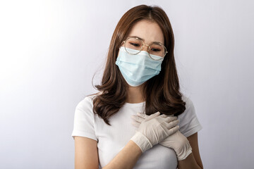 A young worry Asian woman with glasses wearing a face mask and hand gloves to protect the pollution or covid19 virus disease. She touches her heart. Healthcare, virus, and pollution concept