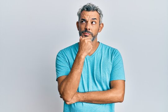 Middle age grey-haired man wearing casual clothes with hand on chin thinking about question, pensive expression. smiling with thoughtful face. doubt concept.