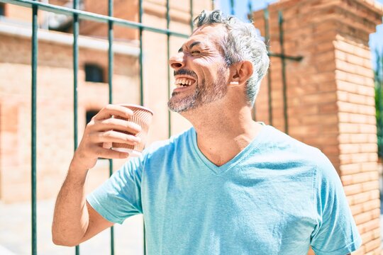 Middle age grey-haired man drinking take away coffee walking at street of city.